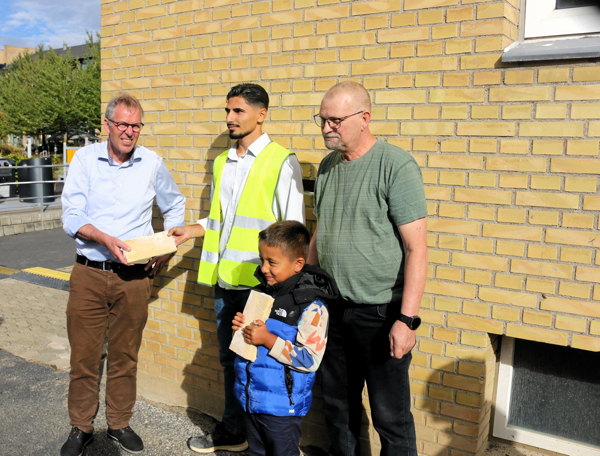 Borgmester Knud Vincents, byggeleder Yasin Can fra Jorton, afdelingsformand Per Glundø og Younes med de to mursten, som er blevet pillet ud af den boligblok, der som den første skal rives ned.