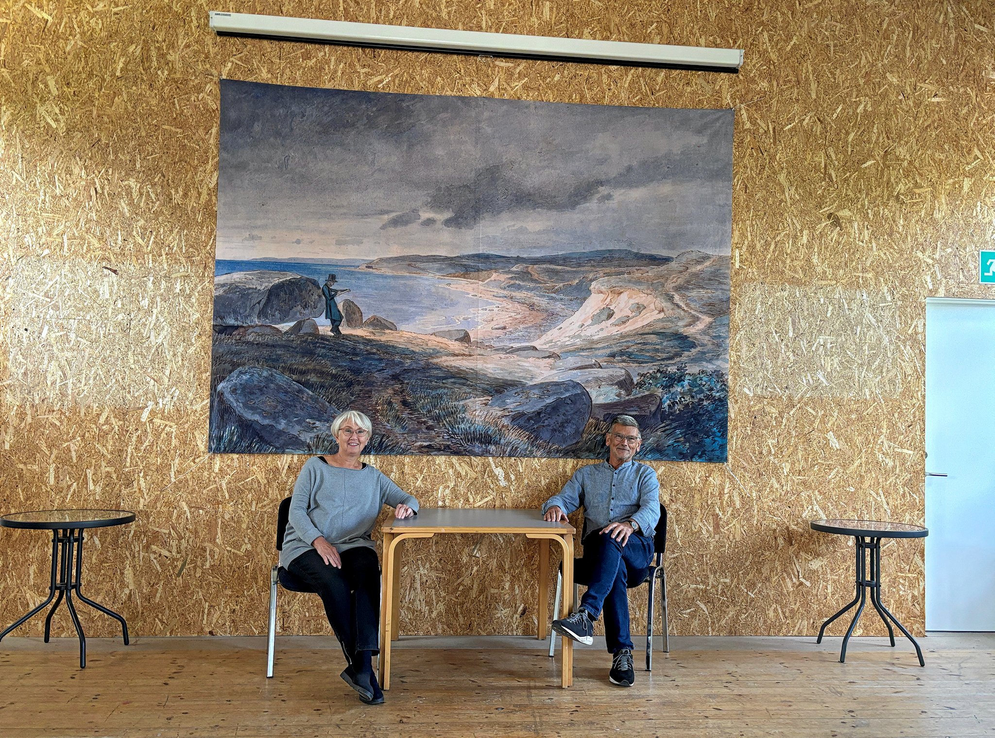 Lene Henrichsen og Troels Birk Kristoffersen sidder under J. Th. Lundbyes billede Refnæs, som blev lavet i forbindelse med Lundbyefestivalen og som Røsnæs Forsamlingshus nu vil købe.