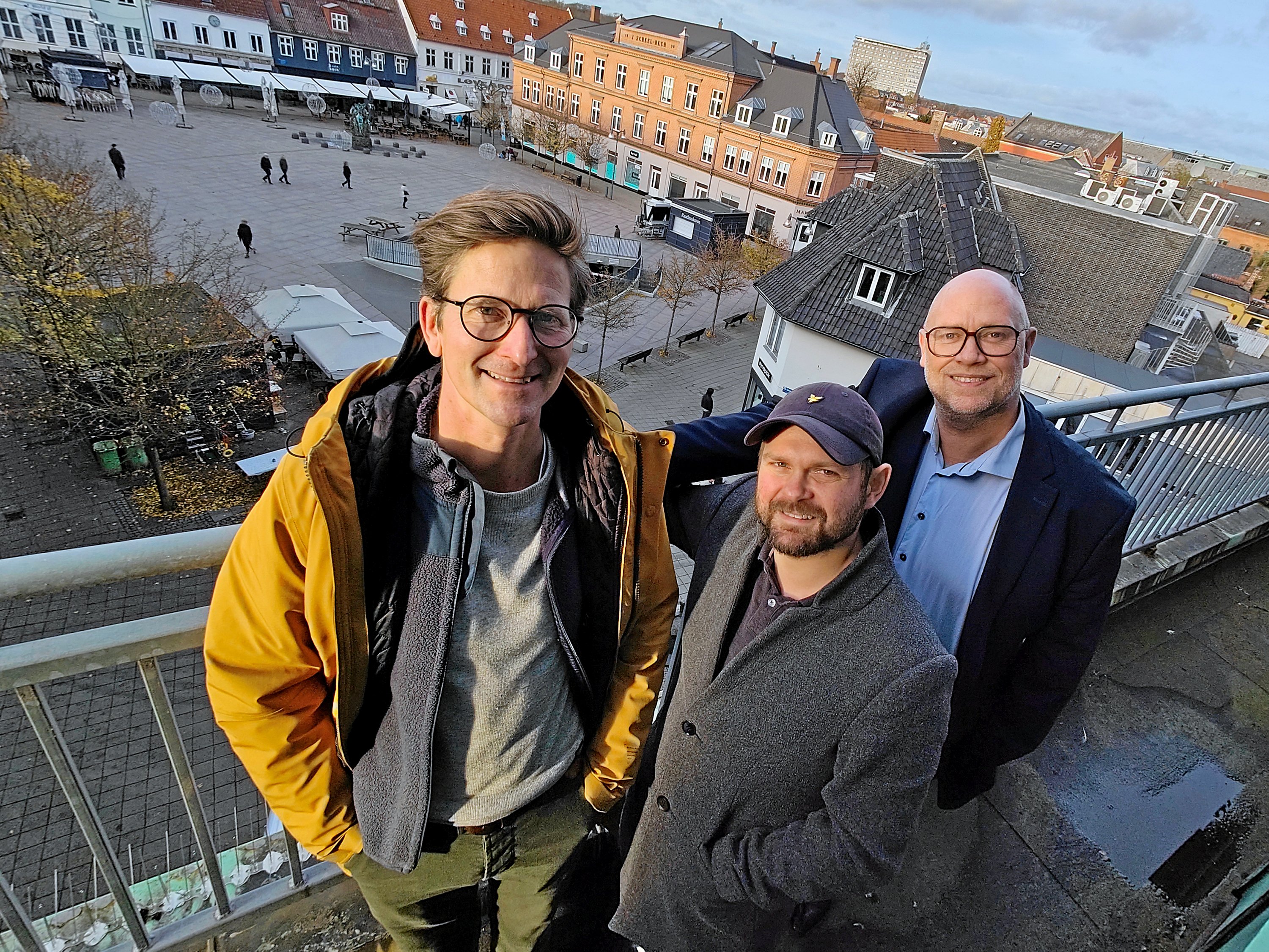 Næstved Cityforening gentager sidste års succes, og bliver klar med skøjtebane på torvet 29. november. På billedet ses citychef Nicolaj Lund Jensen (tv), city's marketingkoordinator René Jørgensen og Sydbanks områdedirektør Kasper Bæk. Han repræsenterer skøjtebanens hovedsponsor på toppen af bankbygningen.