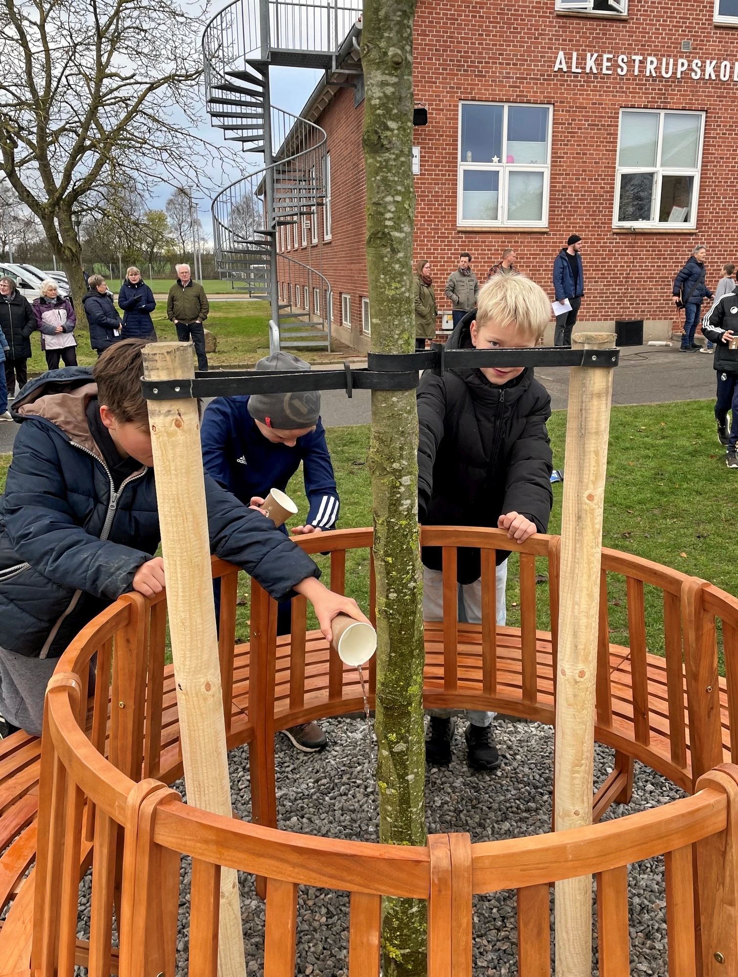 Der blev pøset masser af vand på det nye træ, så det kan gro i fællesskab med skolens elever. - Alkestrupskolen Der blev pøset masser af vand på det nye træ, så det kan gro i fællesskab med skolens elever.