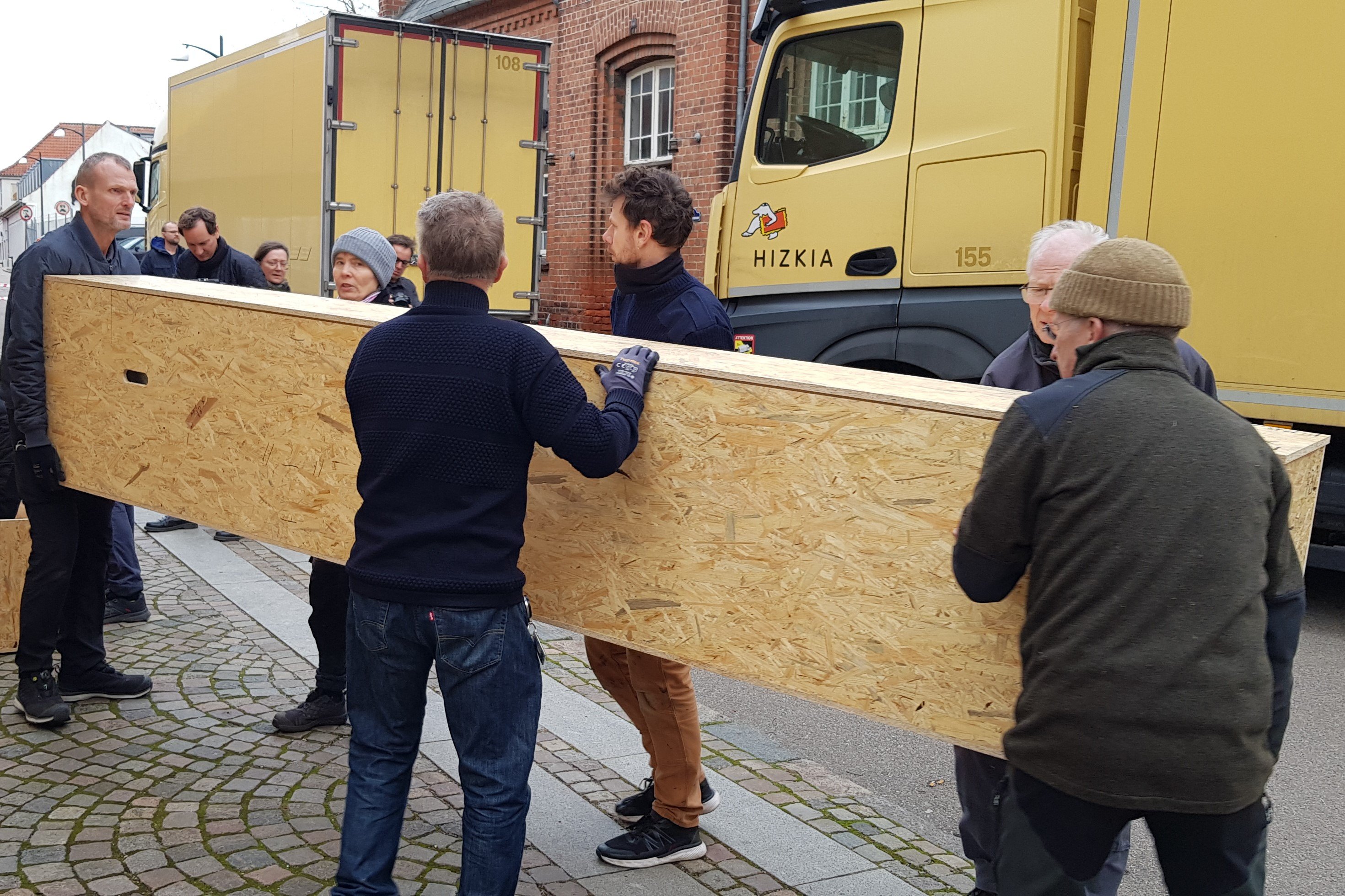 Ansatte fra Museum Vestsjælland og Nationalmuseet bærer de lange kasser med Gislingebådens dele ind fra de gule special-transportbiler.