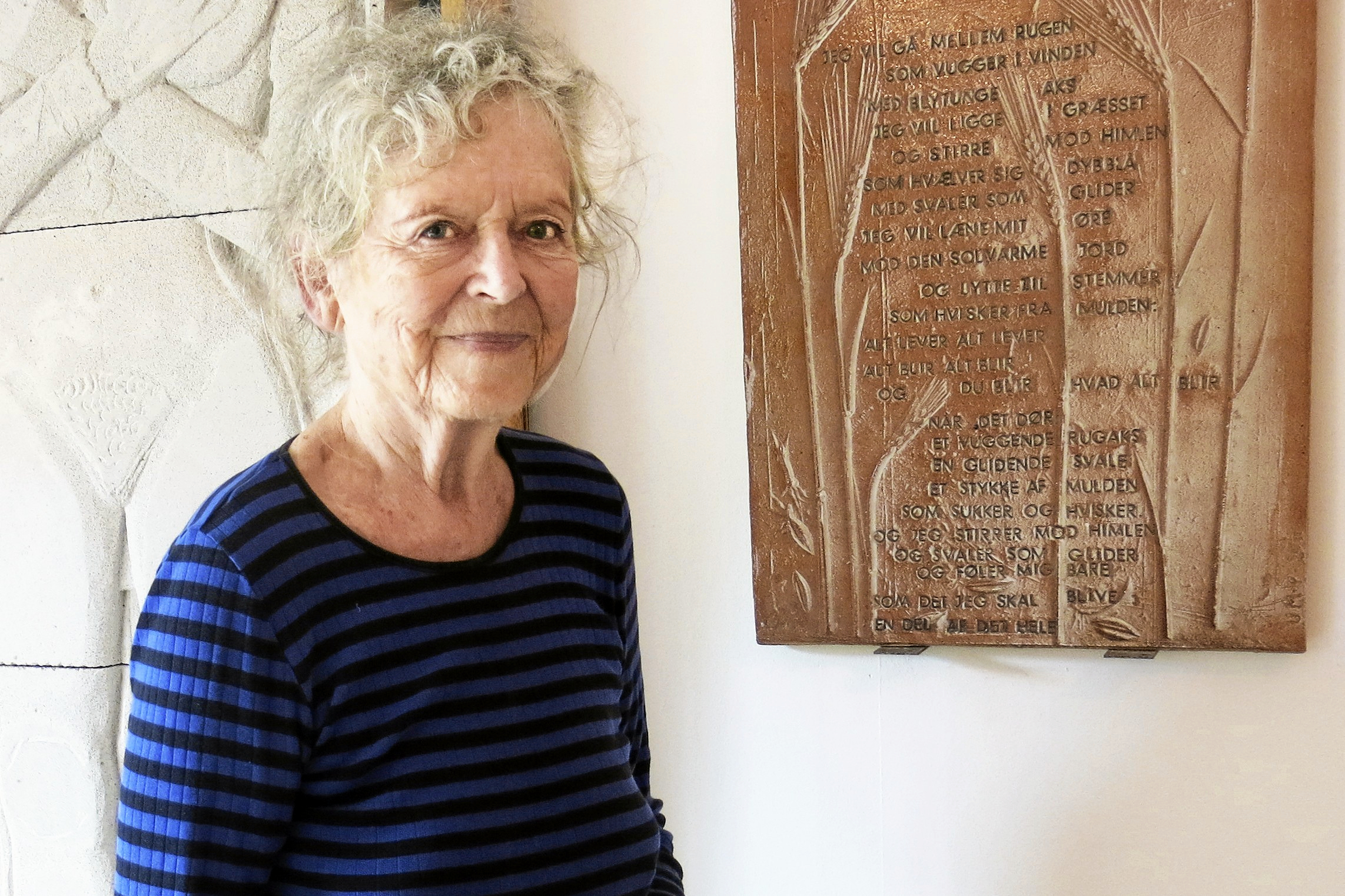 Ursula Munch-Petersen foran et af hendes relieffer, der hænger i Hårbøllehuset.