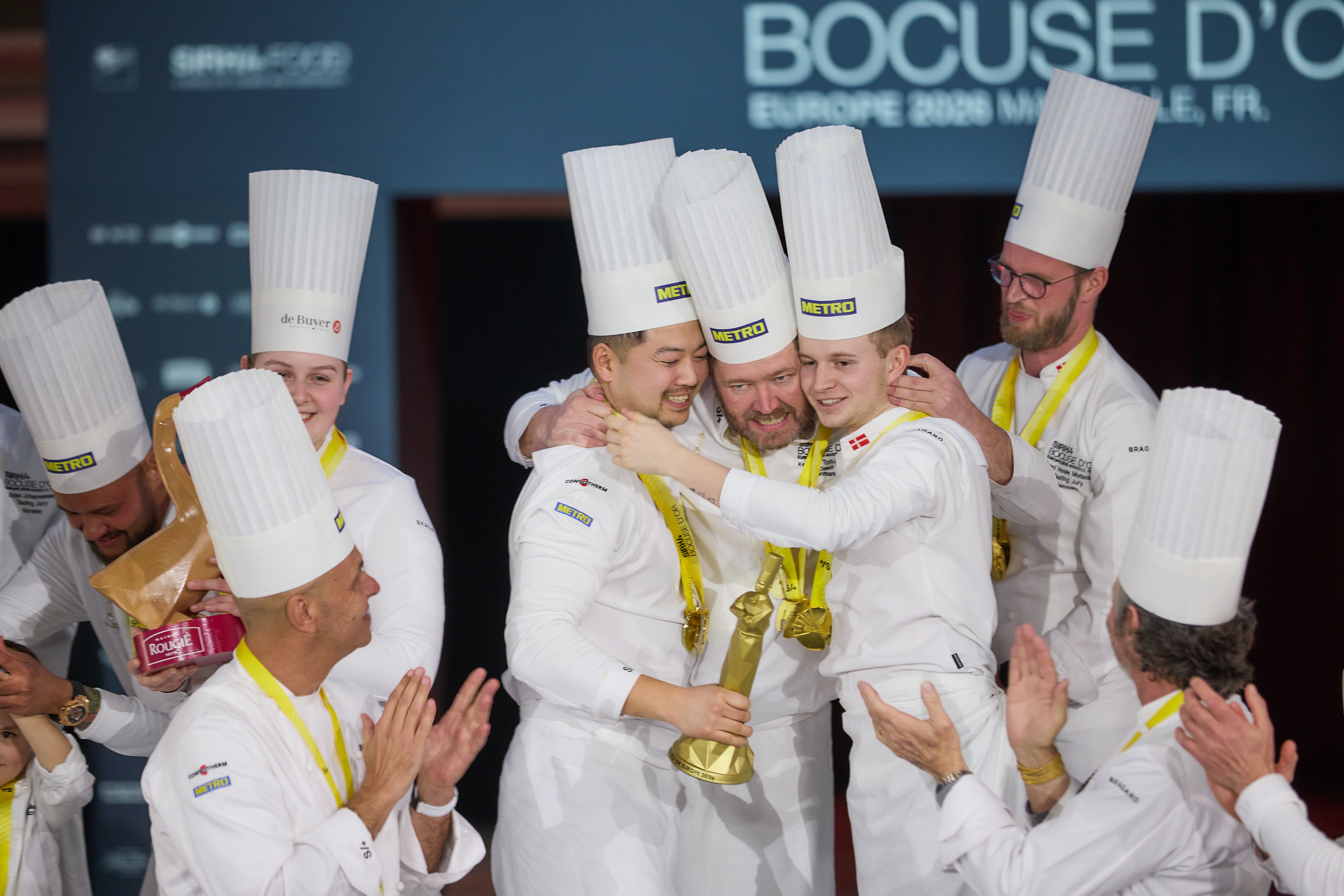 Det danske hold med kok Christian Wellendorf (med statuettee i hånden) i spidsen og Gustav Spurré (th) som commis vandt Bocuse d'Or Europe 2026 i Marseilles. Holdcoach står i midten af de tre.