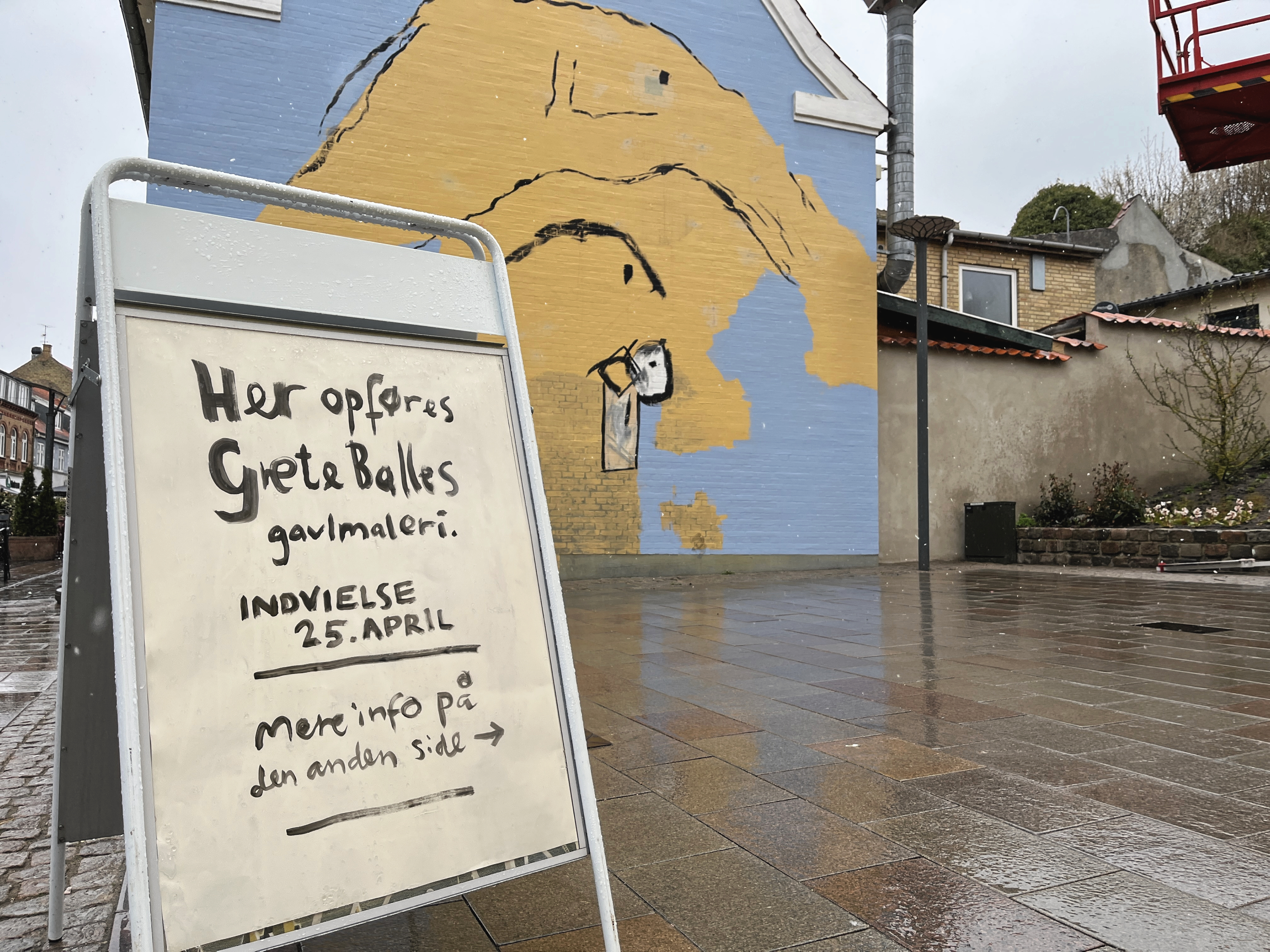 Regn og slud gjorde fredag formiddag, at der måtte holdes en midlertidig pause i arbejdet på Solskinspladsens nye kunstværk, men ellers står billedkunstner Anne Bundgaard parat med penslen til at genskabe Grete Balles maleri, så snart vejret tillader det.