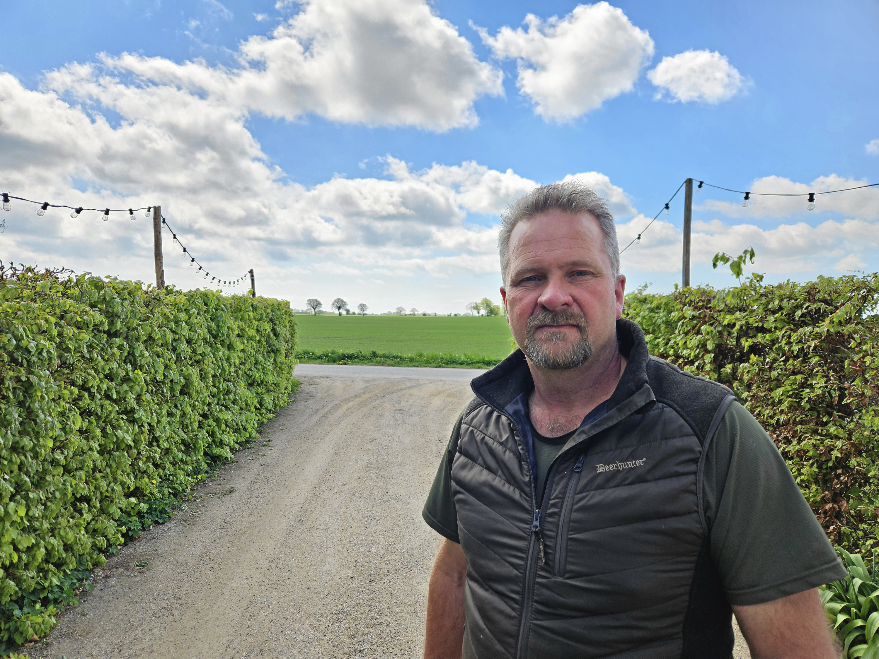 Anders Lund Nielsen i sin indkørsel på Sortevej. Sydstevns Energifællesskab påtænker at placere vindmøller et stykke ude på marken ved Storemarksgård bag ham.