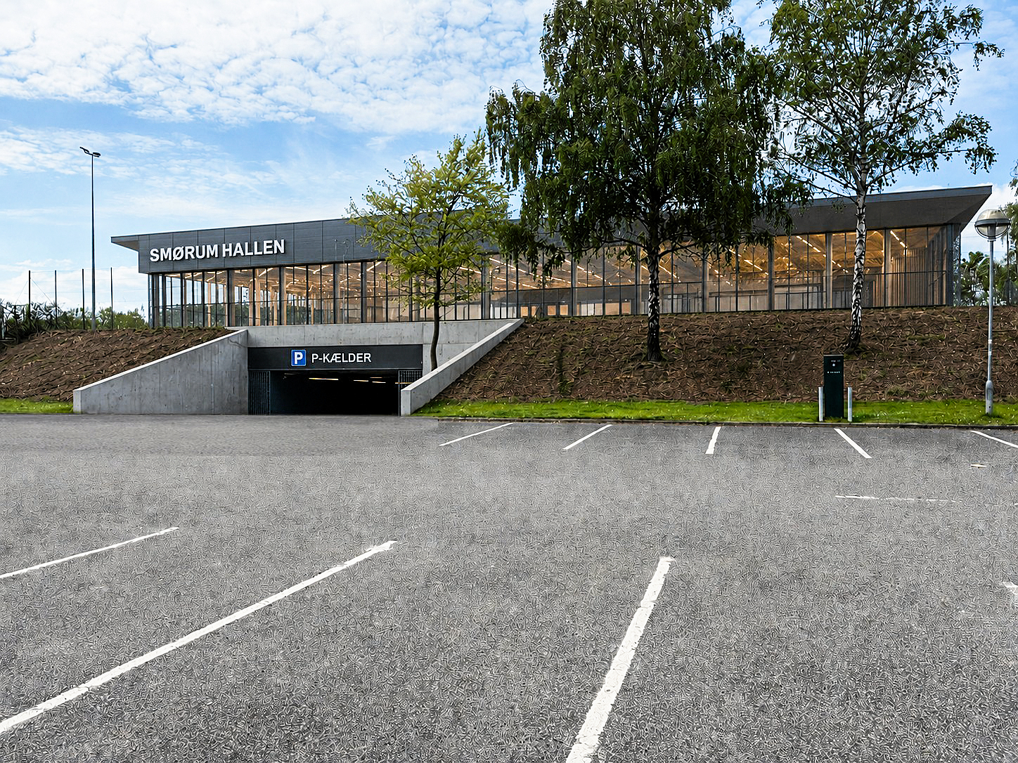 Mit enkle forslag er, at der i stedet udgraves i skråningen ind under den eksisterende højtliggende træningsbane placeret umiddelbart ved hallens nuværende p-pladser. Herpå bygges der en stor arkitekttegnet hal/haller ovenpå en ny underliggende parkeringskælder, skriver Peter Andersen fra Smørum, som her illustrerer sin idé.