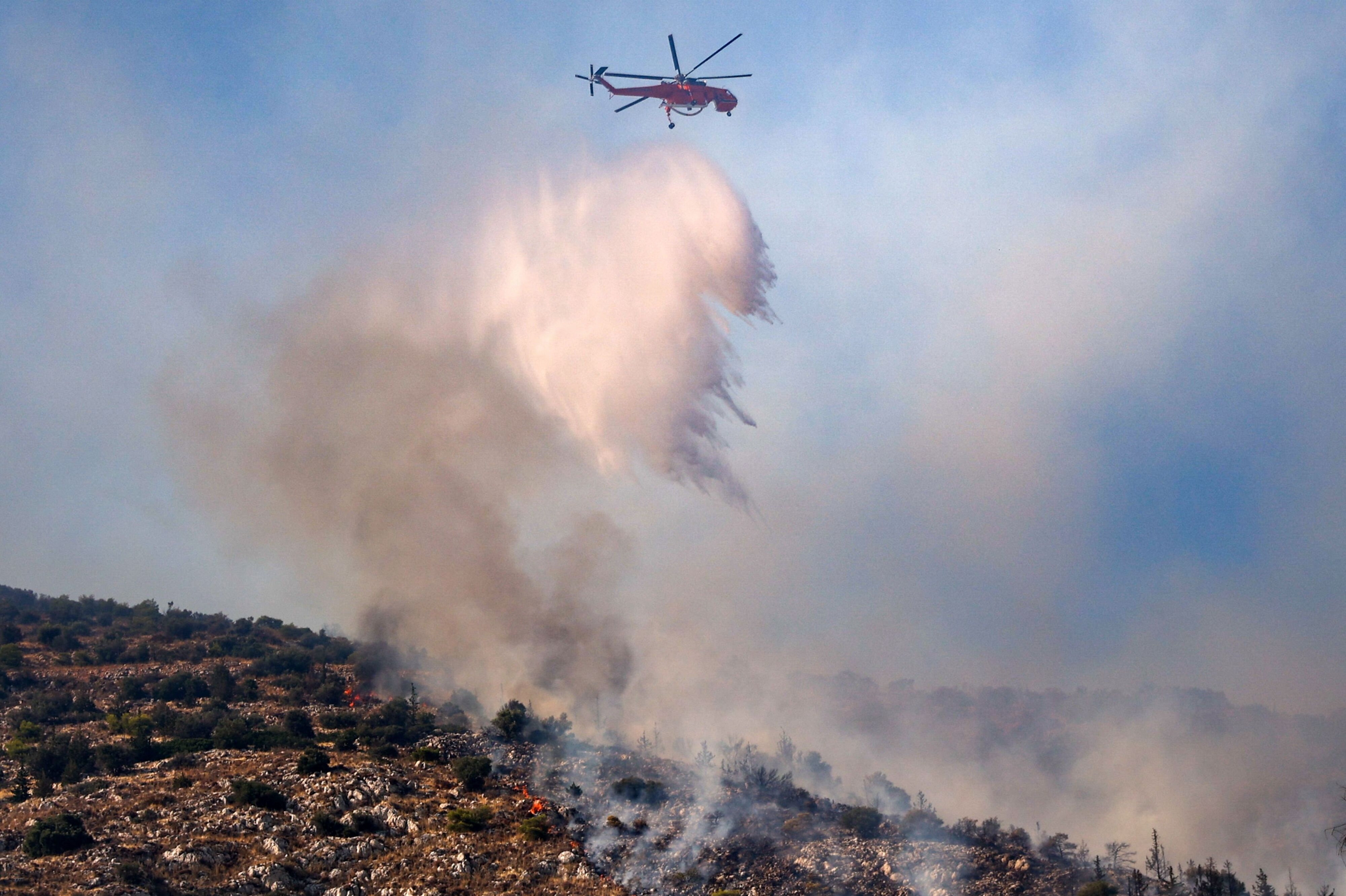 En af det græske brandvæsens helikoptere kaster vand ned over en brand i Haidari, der ligger vest for Athen.