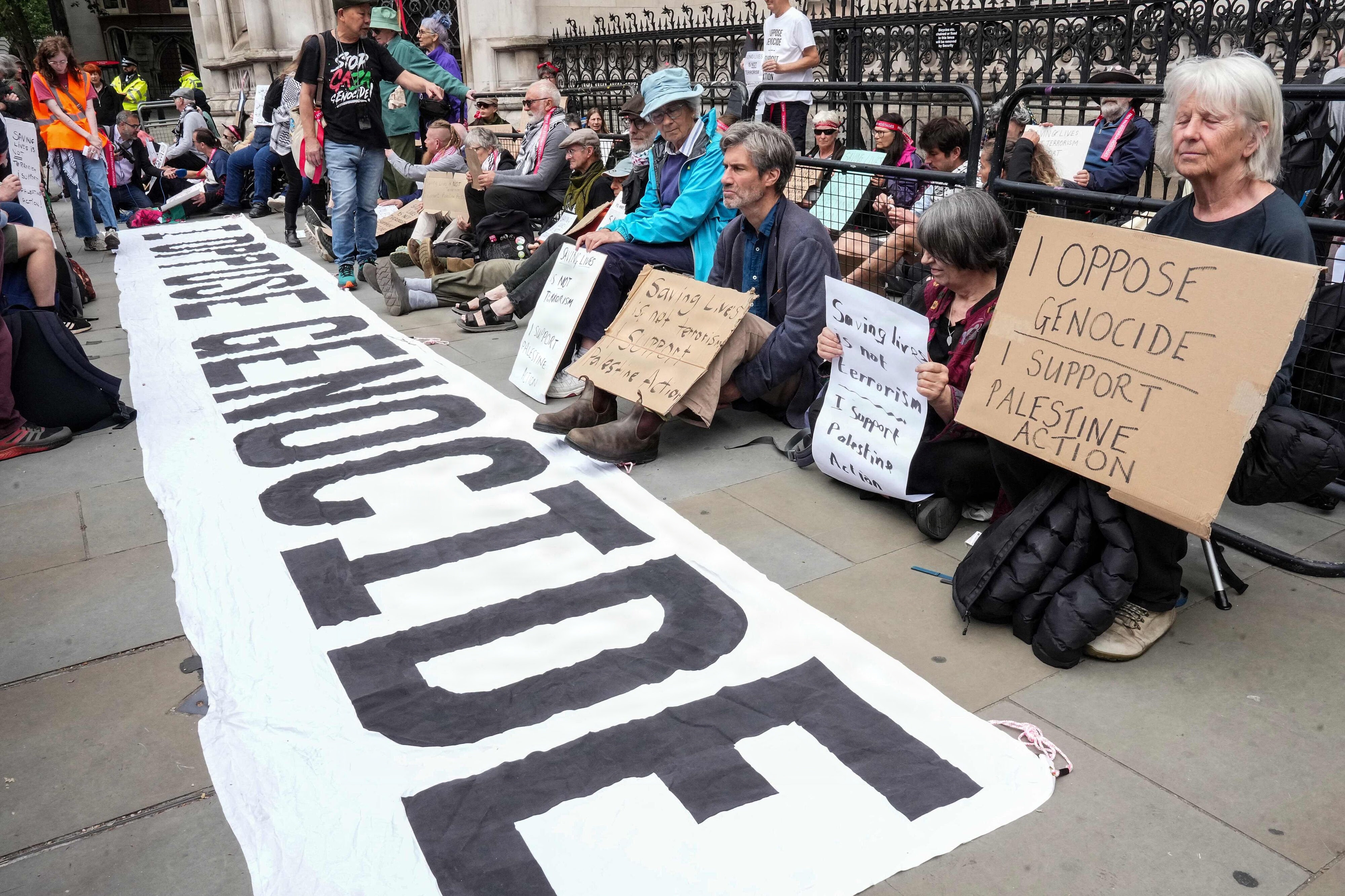 Demonstranter står i juni uden for en britisk domstol i forbindelse med dom i sag om gruppen Palestine Action. På et banner står: "Jeg er imod folkedrab". (Arkivfoto).