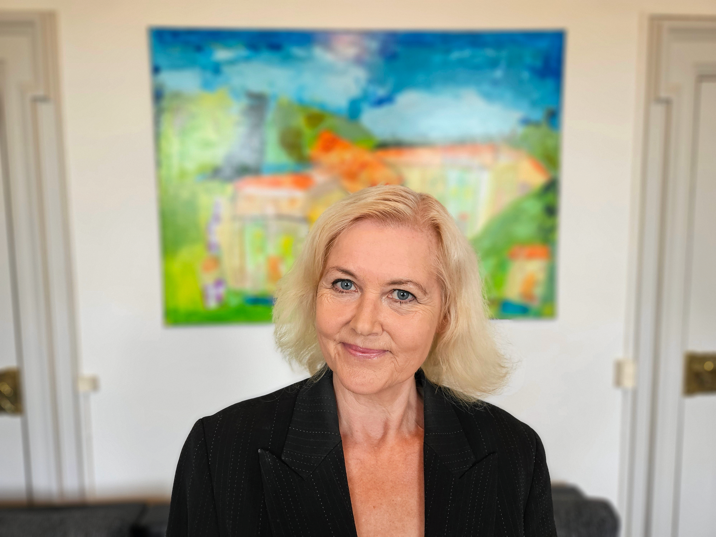 Forfatter Anne-Marie Vedsø Olesen på Vallø Slot i forbindelse med udgivelsen af "Jul i Jernskoven", september 2026. Bag hende ses maleriet "Himlinge", som billedkunstner Jørgen Jungersted, der også bor på Vallø Slot, har malet med inspiration i "Vølvens vej".