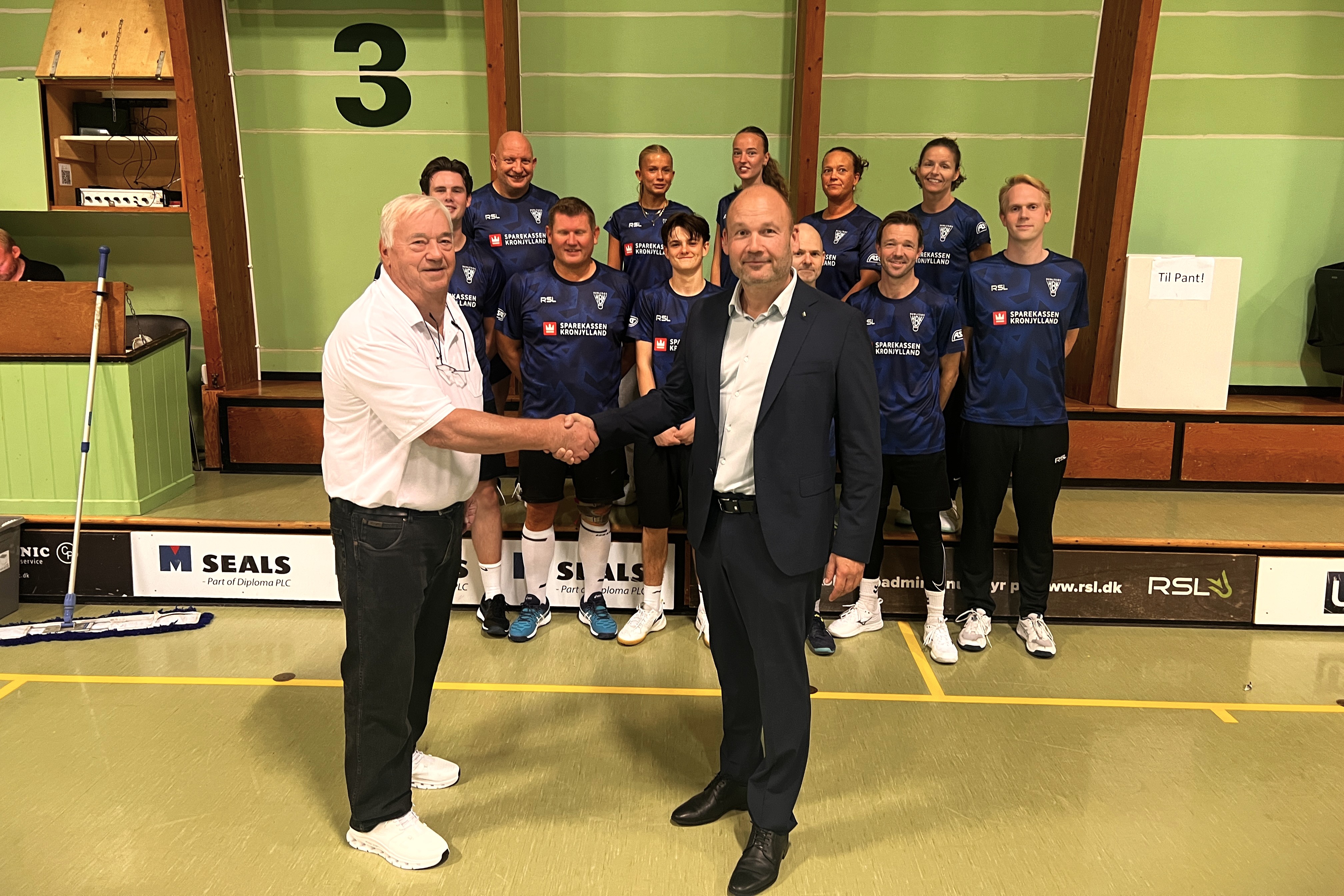 Afdelingsdirektør Preden Blauenfeldt trykker hånd med formand for Humlebæk Badminton Klub Henrik Palling (til venstre) foran klubbens 3. divisionshold.