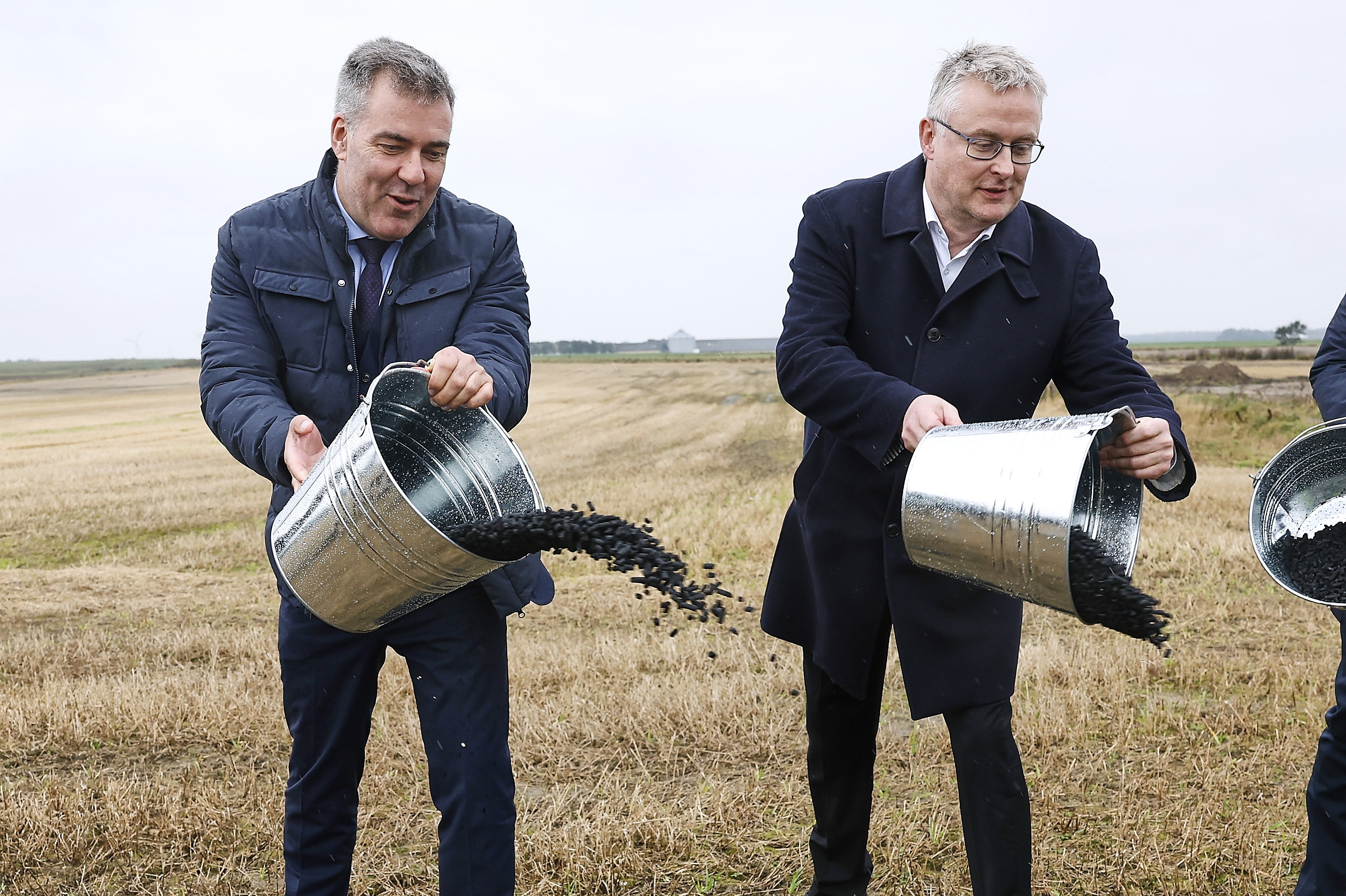 Den tidligere klimaminister Lars Aagaard (tv) og den tidligere landbrugsminister Jacob Jensen (th) spreder her biokul ved en åbning af en fabrik i 2024. (Arkivfoto).